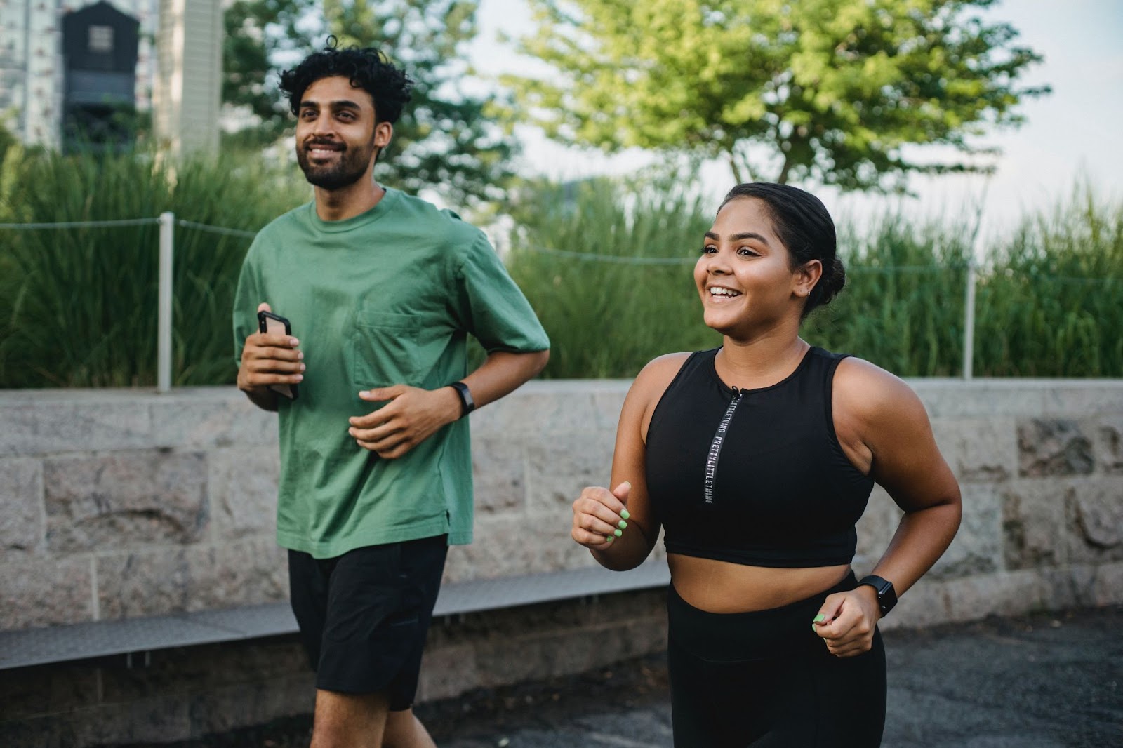 Two joggers outdoors: a man in green with a phone and a smiling woman in black sportswear.