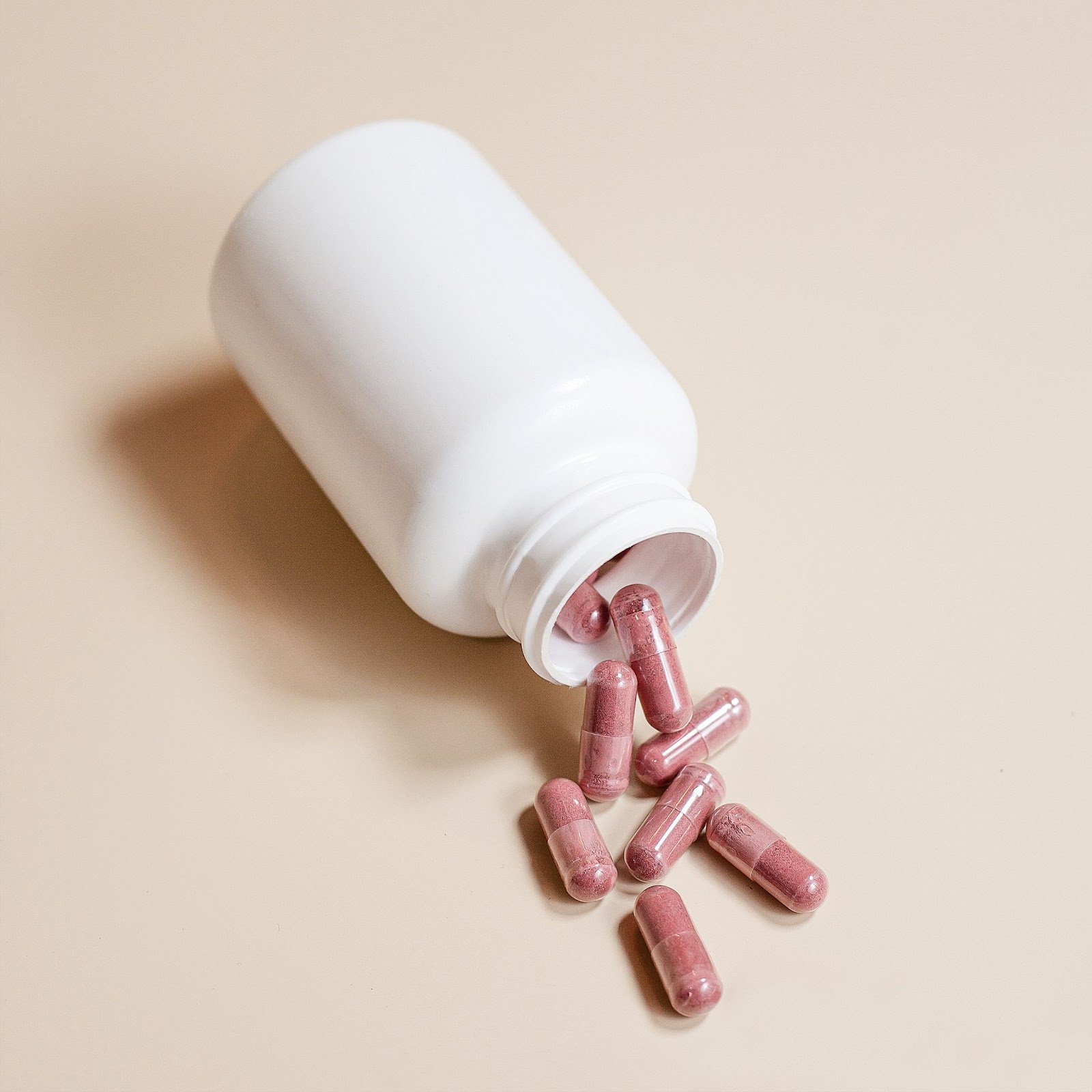 A white pill bottle tipped over, with Resveratrol capsules spilling out onto a beige background.