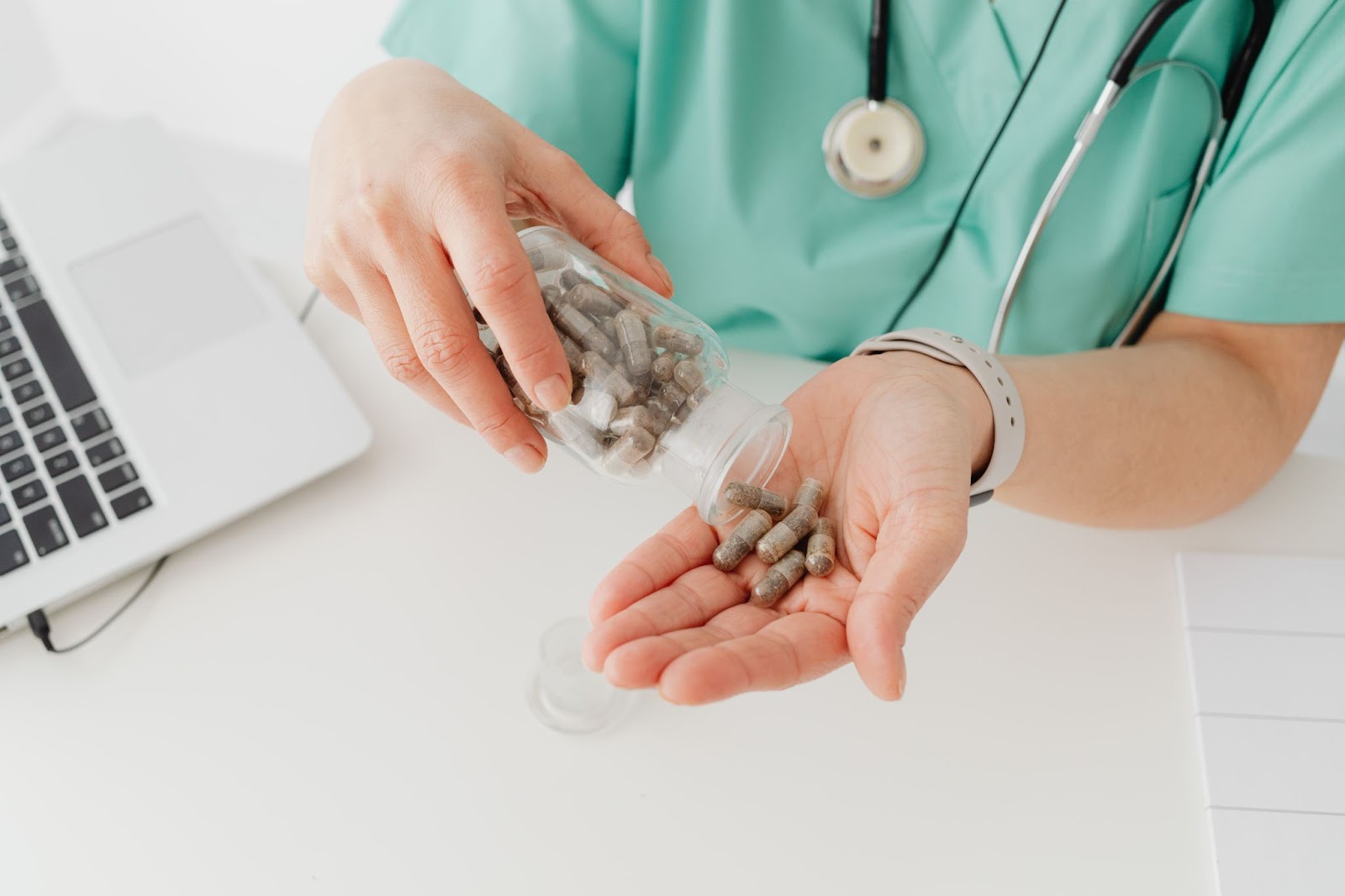 Doctor in teal scrubs pouring capsules from a bottle.