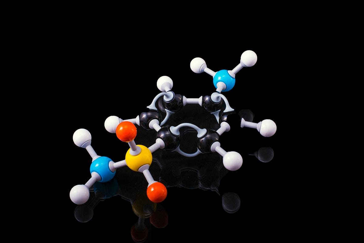 A 3D molecular structure with white, black, blue, yellow, and orange atoms connected by grey bonds