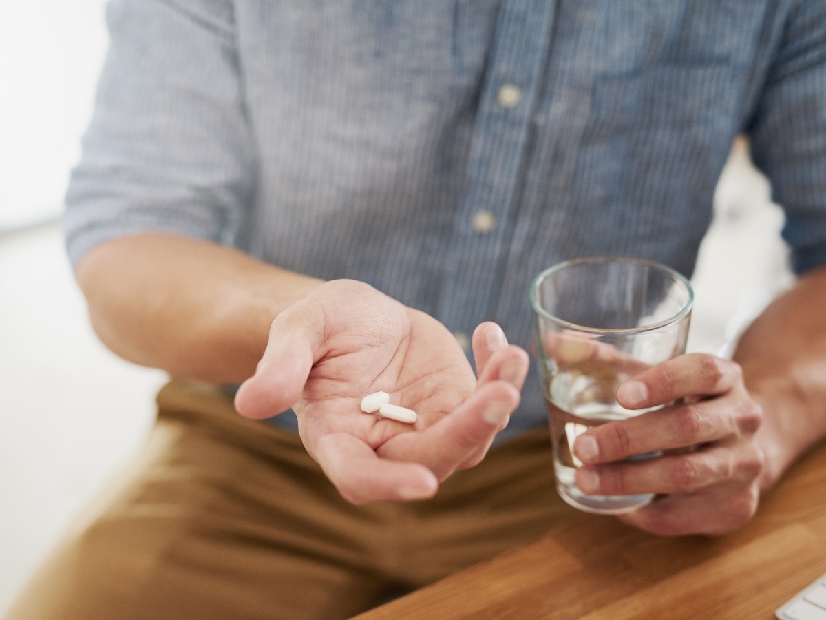 A man holding two ashwagandha pills and a glass of water