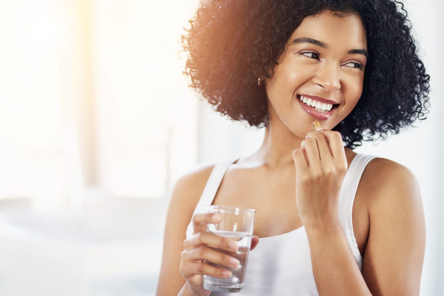 A young woman holding a glass of water and resveratrol supplement